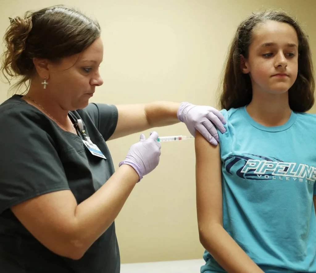 Healthcare professional administering vaccination to young patient in examination room.