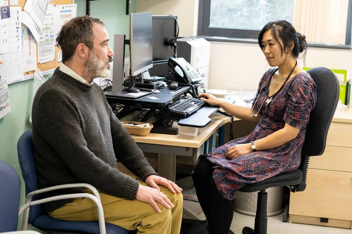 Doctor consulting with patient across desk in clinic office.