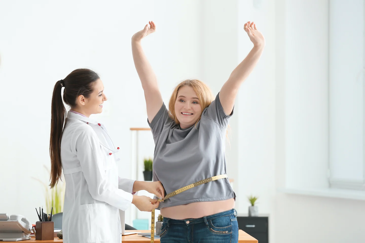 Healthcare professional measuring patient’s waist circumference with tape in consultation room.