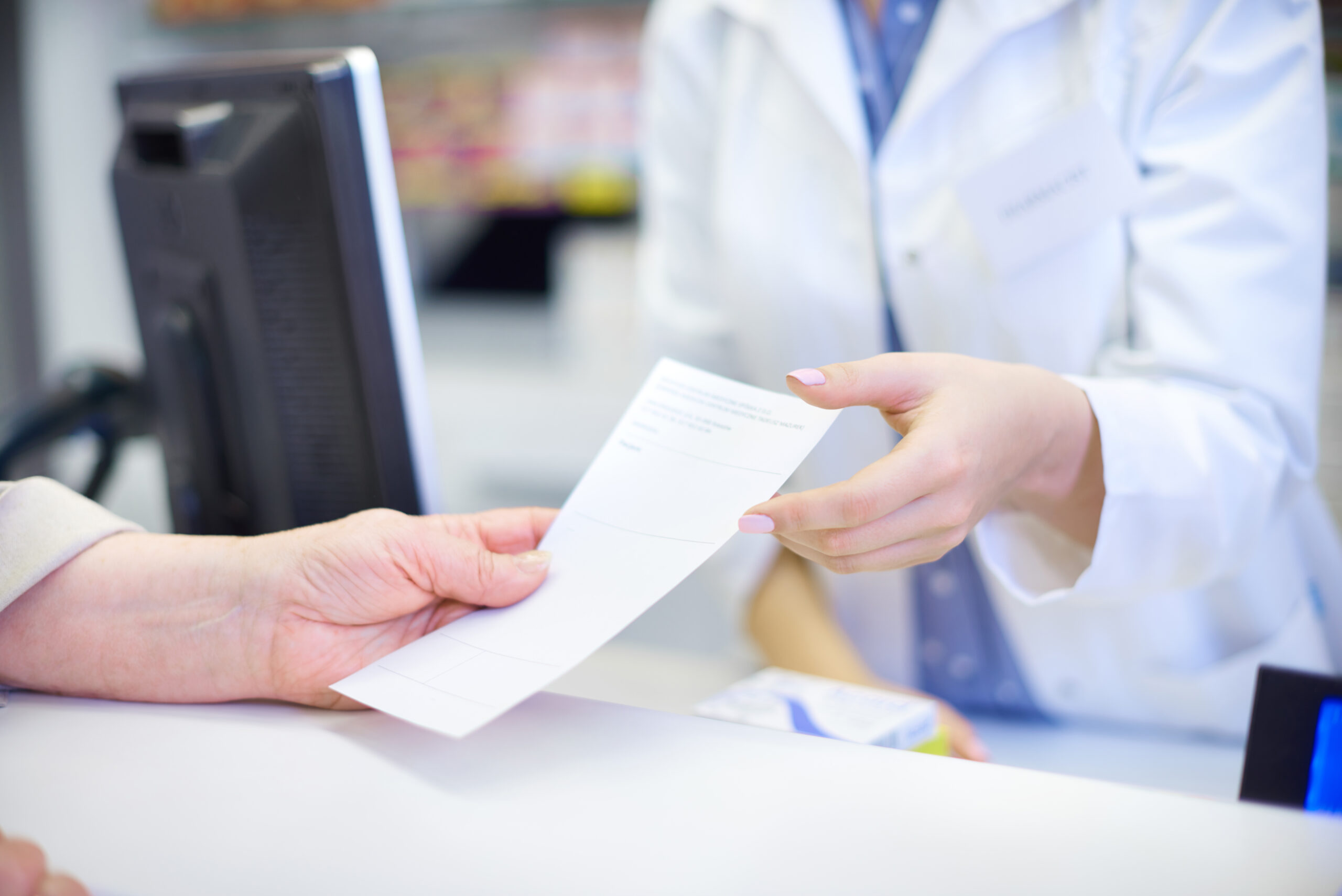 Pharmacist handing a prescription document to a customer at Kingsland Pharmacy, Mary Street, Southampton.
