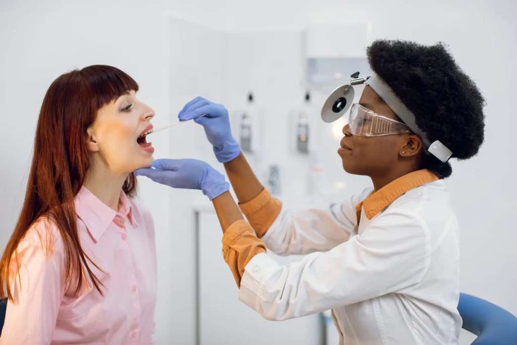 Medical professional performing oral examination with tongue depressor and protective eyewear.