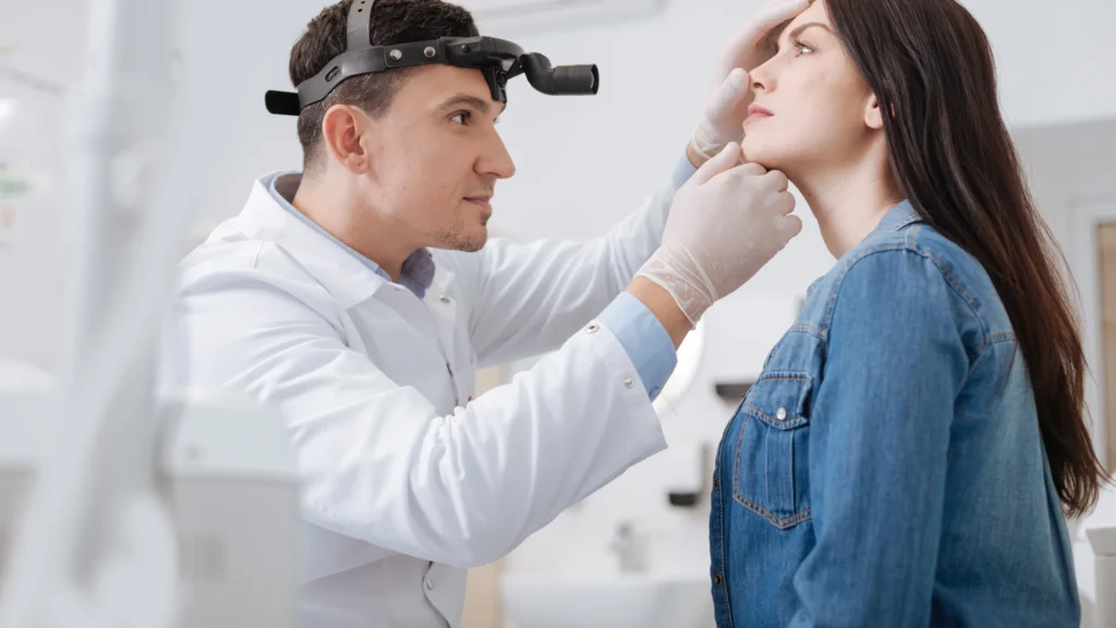 A healthcare professional inspects a patient’s face in a clinical setting.