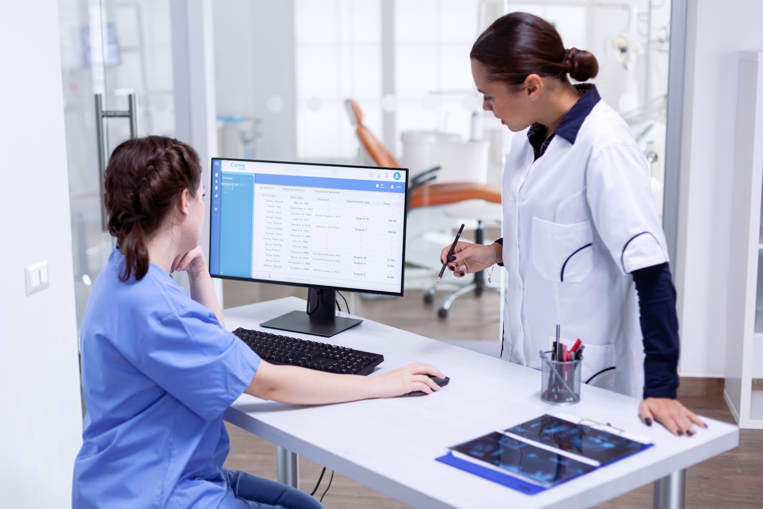 Healthcare staff collaborating at a computer to manage patient appointments and medical records.