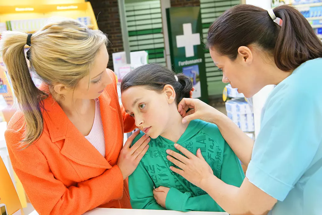 A healthcare professional examines a young person’s ear in a pharmacy setting, observed by a companion at Kingsland Pharmacy, Mary Street, Southampton.